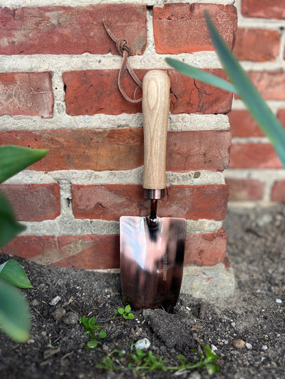 Kobber haveskovl med træhåndtag, der står op ad en murstensmur