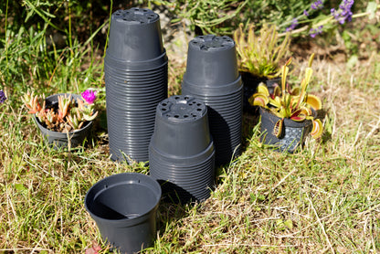 Sorte plastikpotter stablet oven på hinanden med lidt planter i baggrunden